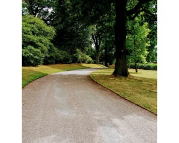 A winding wide gravel path curves through a green park with large trees and manicured lawns, creating a peaceful, shaded outdoor setting perfect for showcasing PROEDGE.