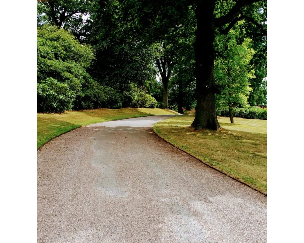 EverEdge PROEDGE Landscape Edging – 1 A winding wide gravel path curves through a green park with large trees and manicured lawns, creating a peaceful, shaded outdoor setting perfect for showcasing PROEDGE.