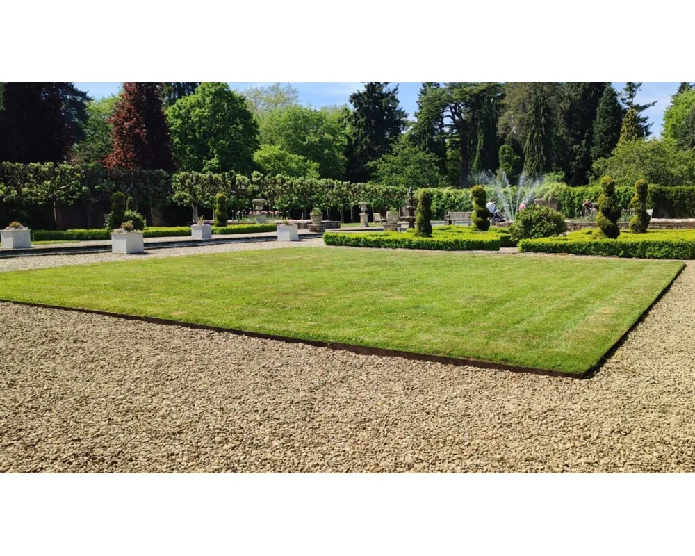 EverEdge PROEDGE Landscape Edging – 8 A neatly manicured grassy square, bordered by gravel paths and low hedges, features PROEDGE topiary bushes, white planter boxes, and trees in the background on a bright, sunny day.